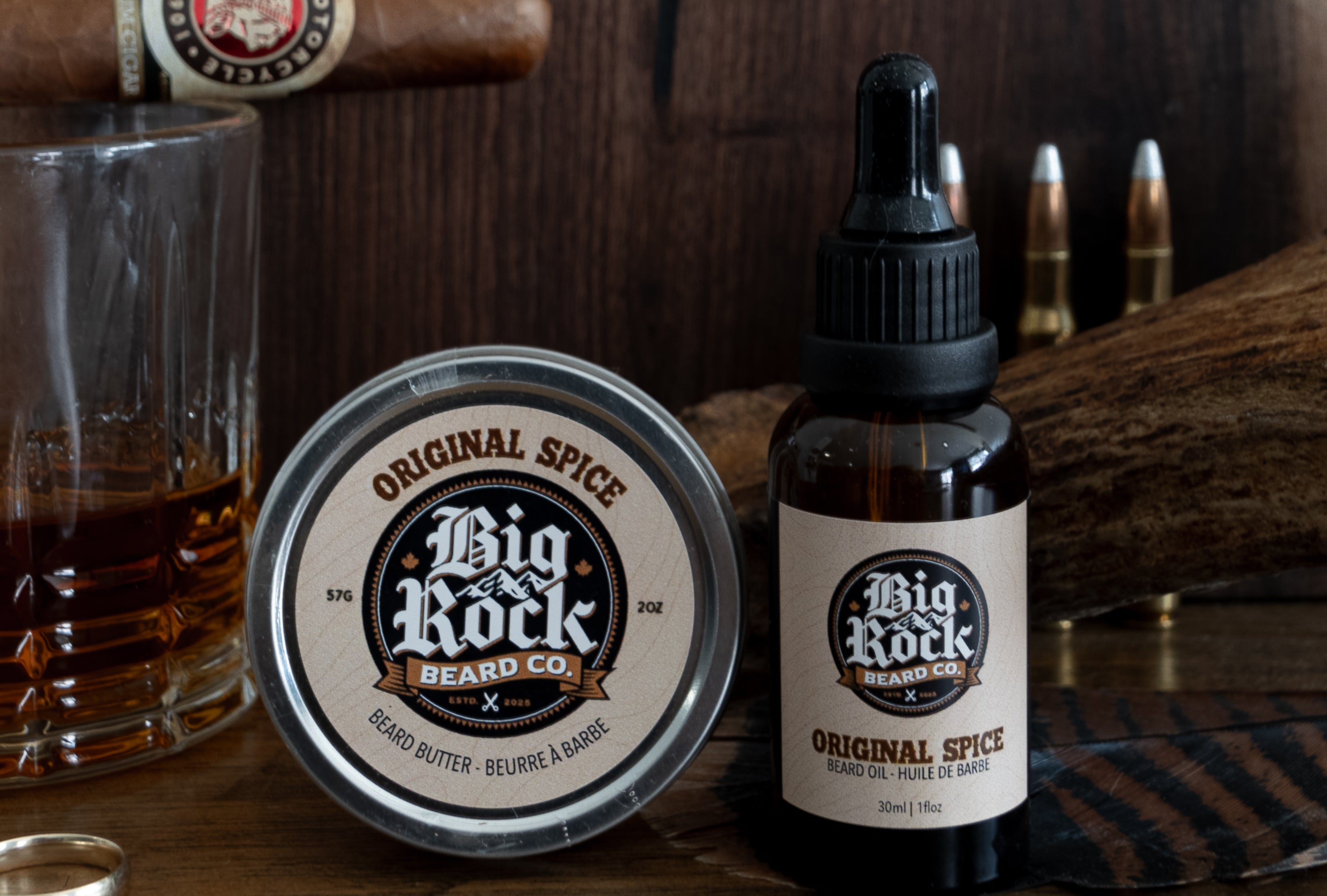 Big Rock beard care products on a wooden surface with a cigar and glass of whiskey.